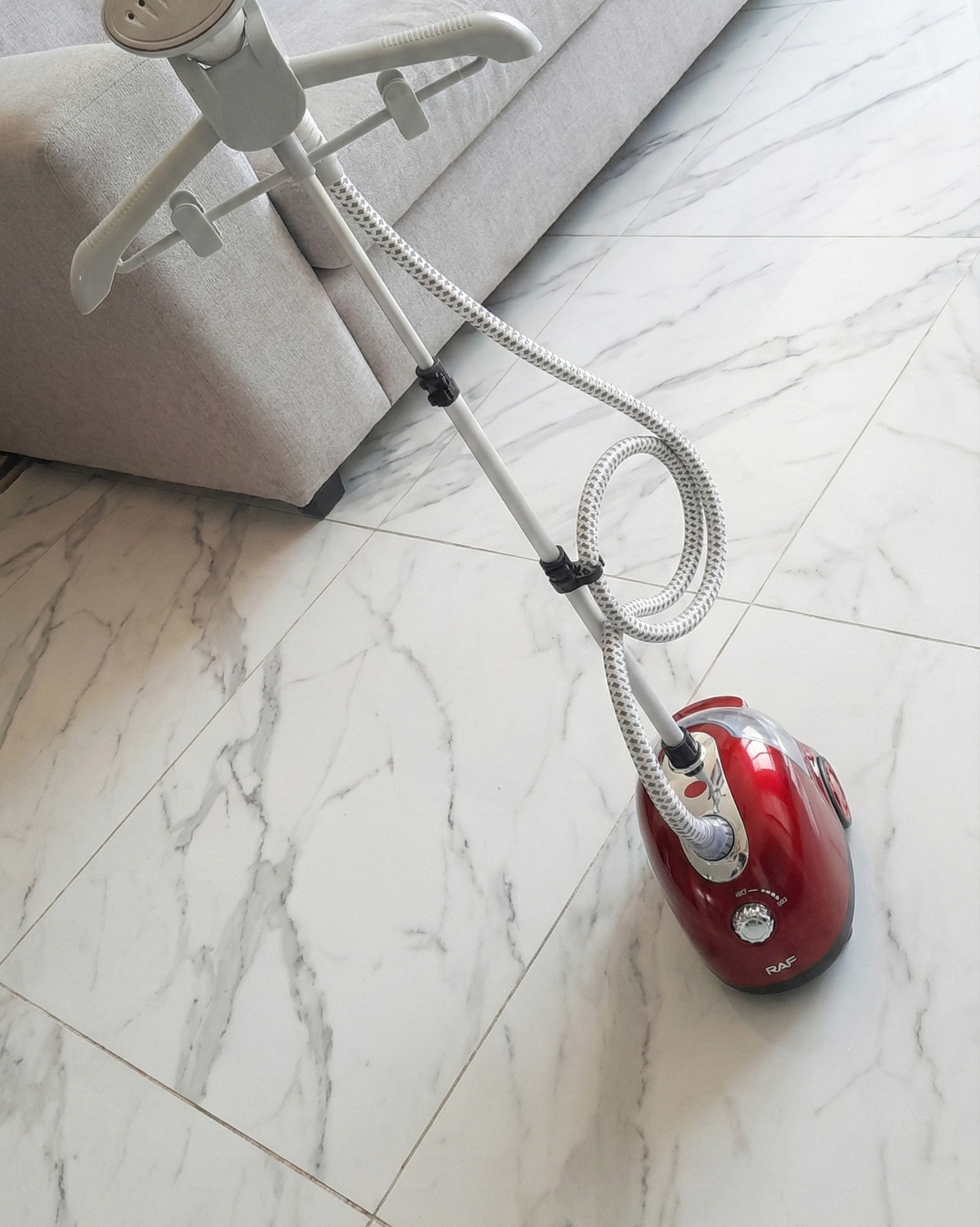 Red vacuum cleaner on a marble floor with a white sofa in the background