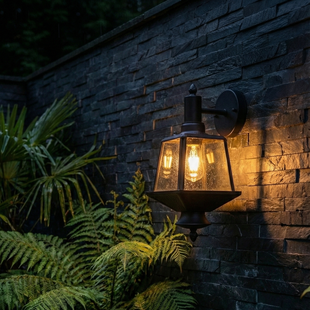 Outdoor wall-mounted light fixture illuminating a stone wall and plants