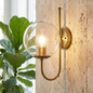 Wall-mounted light fixture with a glass shade on a textured wall next to a plant.
