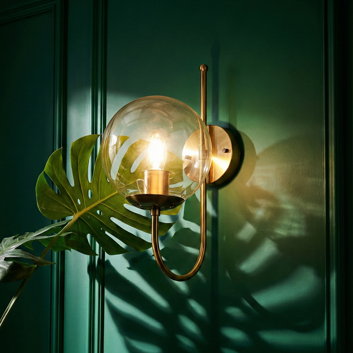 Wall-mounted lamp with a glass shade on a green wall, casting shadows.